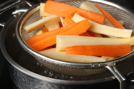 Sieve with cut parsnips and carrots over pot of boiling water, closeupの写真素材