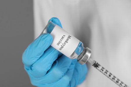 Nurse filling syringe with monkeypox vaccine from glass vial on gray background, closeupの写真素材