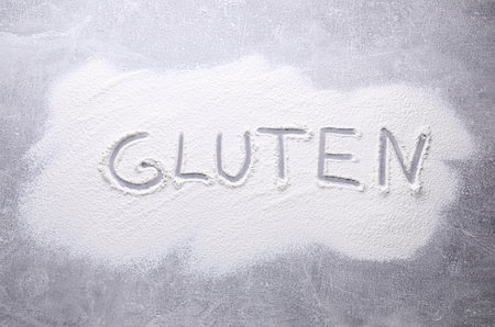 Word Gluten written with flour on gray background, top viewの写真素材