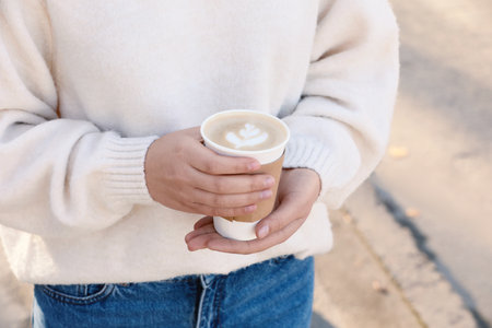 Woman holding takeaway cardboard cup on city street, closeup. Coffee to go
