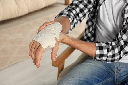 Man with hand wrapped in medical bandage indoors, closeupの写真素材