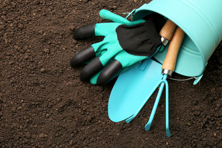 Overturned bucket with gardening tools and gloves on fresh soil, flat lay. Space for textの写真素材