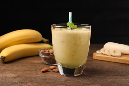 Glass with banana smoothie and mint on wooden table against black backgroundの写真素材