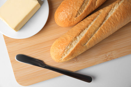 Tasty baguettes with fresh butter on white table, top view