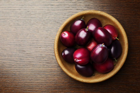 Bowl with tasty ripe plums on wooden table, top view. Space for textの写真素材