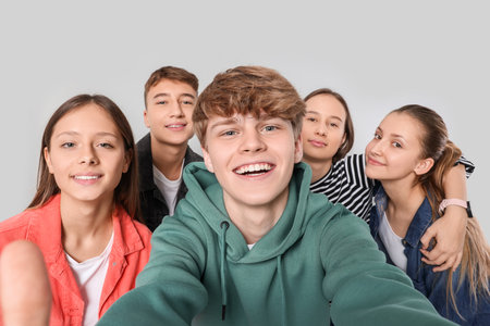 Group of happy teenagers taking selfie on light gray background