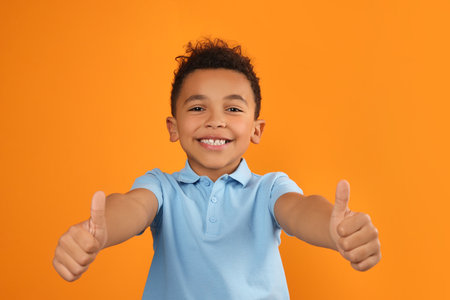 African-American boy showing thumbs up on orange backgroundの写真素材