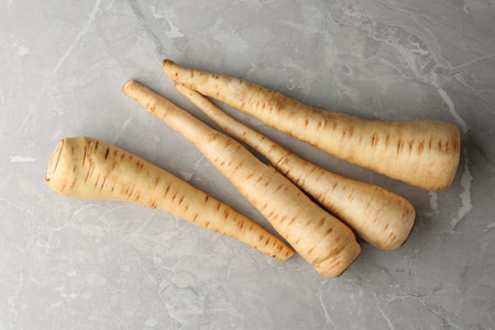 Many fresh ripe parsnips on gray marble table, flat lay
