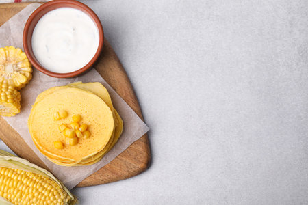 Tasty corn pancakes with sweet kernels and sauce served on light gray table, flat lay. Space for textの写真素材