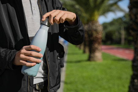 Man holding thermo bottle in park on sunny day, closeup. Space for textの写真素材
