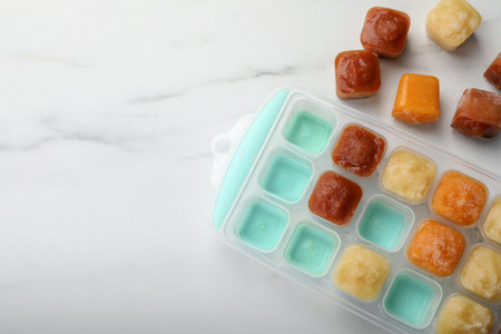 Different fruit puree in ice cube tray on white marble table, flat lay. Space for textの写真素材