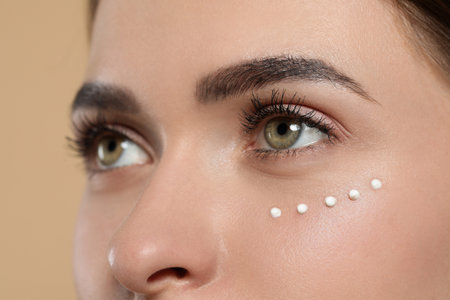 Young woman with cream around eye on beige background, closeupの写真素材