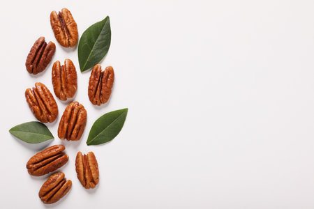 Delicious pecan nuts and green leaves on white background, flat lay. Space for textの写真素材