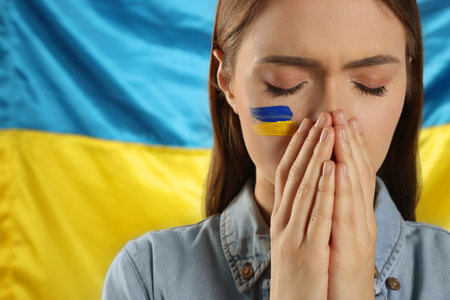 Sad young woman with clasped hands near Ukrainian flag, closeup. Space for textの写真素材