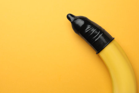 Banana with condom on orange background, top view and space for text. safe sex conceptの写真素材