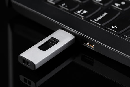 Modern usb flash drive attached to laptop on black table, closeup