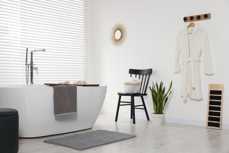 Stylish bathroom interior with ceramic tub, terry towels and houseplant
