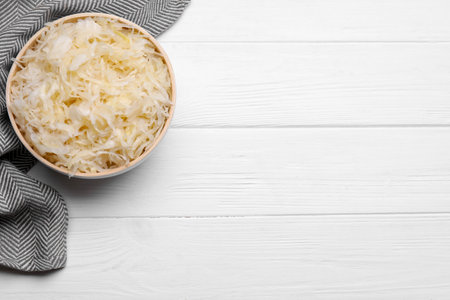 Bowl of tasty sauerkraut on white wooden table, flat lay. Space for text