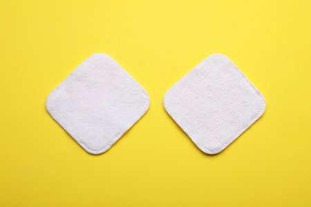Soft clean cotton pads on yellow background, flat lay