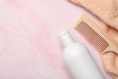 Shampoo bottle, wooden comb and towel on pink marble table, flat lay. Space for text