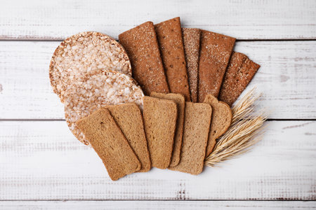 Rye crispbreads, rice cakes and rusks on white wooden table, flat lay