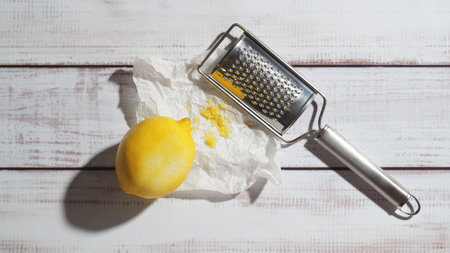 Lemon, grater and paper with fresh zest on white wooden table, top viewの写真素材