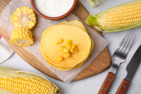 Tasty corn pancakes with sweet kernels and sauce served on light gray table, flat layの写真素材