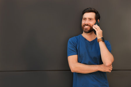 Happy man talking on phone near gray wall. Space for text