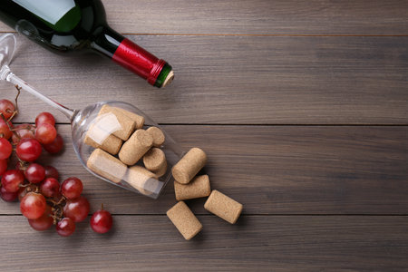 Bottle of wine, glass with corks and grapes on wooden table, flat lay. Space for textの写真素材