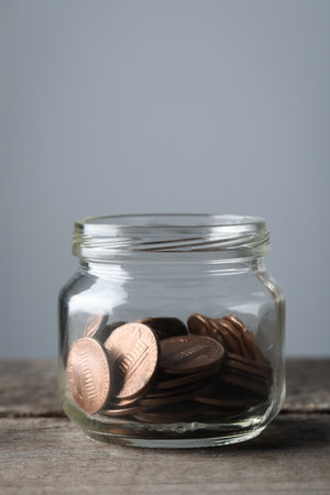 Glass jar with coins on wooden table, closeup