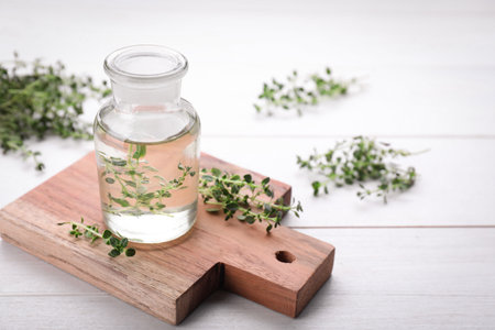 Bottle of thyme essential oil and fresh plant on white wooden table, space for textの写真素材