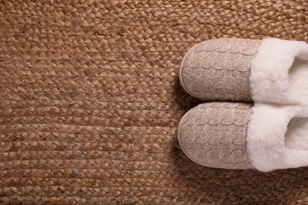 Pair of warm stylish slippers on wicker carpet, top view. Space for text