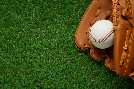 Catcher's mitt and baseball ball on green grass, top view with space for text. sports game
