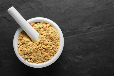 Mortar of mustard powder on black table, top view. Space for text
