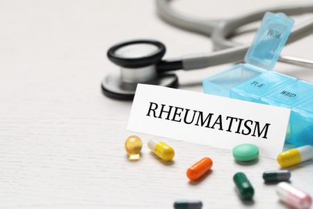 Sheet of paper with word Rheumatism and many different pills on white wooden table, closeup. Space for textの写真素材