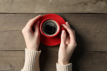 Woman holding cup of aromatic coffee at wooden table, top viewの写真素材