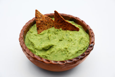 Delicious guacamole made of avocados with nachos on white background, closeup