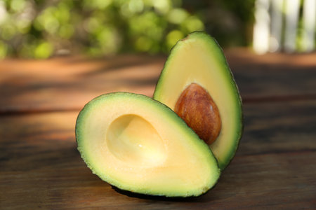 Halves of fresh avocado on wooden table outdoors, closeup