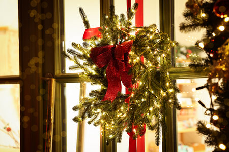 Beautiful Christmas wreath with ribbons and festive lights hanging on door