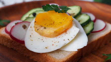Tasty sandwich with boiled egg, radish and cucumber on wooden plate, closeupの写真素材