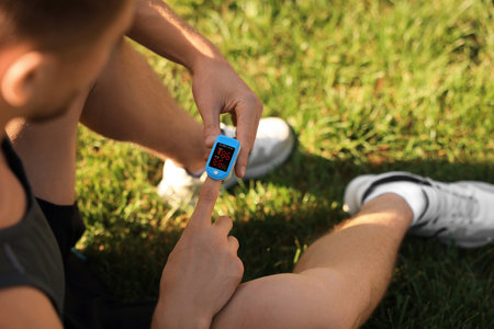 Man checking pulse with blood pressure monitor on finger after training outdoors, closeupの写真素材
