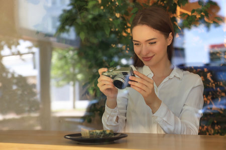 Young woman taking photo of plate with pie at cafe, view through window. creative hobby