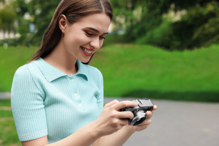 Young woman with camera in park, space for text. interesting hobby