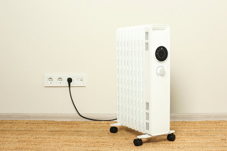 Modern portable electric heater on floor near beige wall indoors, space for textの写真素材