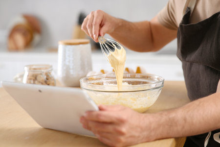 Man making dough while watching online cooking course via tablet in kitchen, closeup