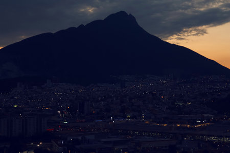 Picturesque view of sunset with dark clouds above big mountains and cityの写真素材