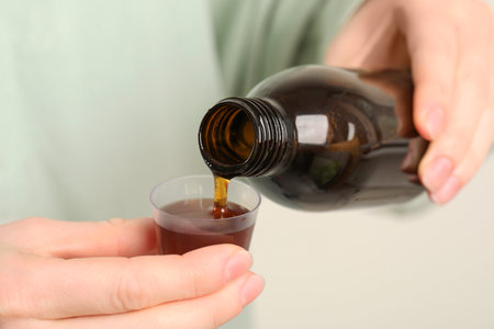 Woman pouring syrup from bottle into measuring cup, closeup. cold medicineの写真素材