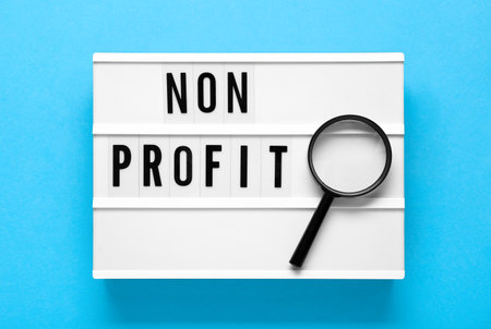 Notebook with phrase Non Profit and magnifying glass on light blue background, top viewの写真素材