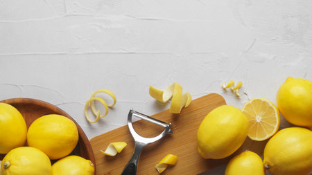 Wooden board, lemons, peeler and fresh rind on white textured table, flat lay. Space for text