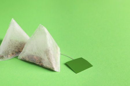 New tea bags with tabs on green background, closeup. Space for textの写真素材